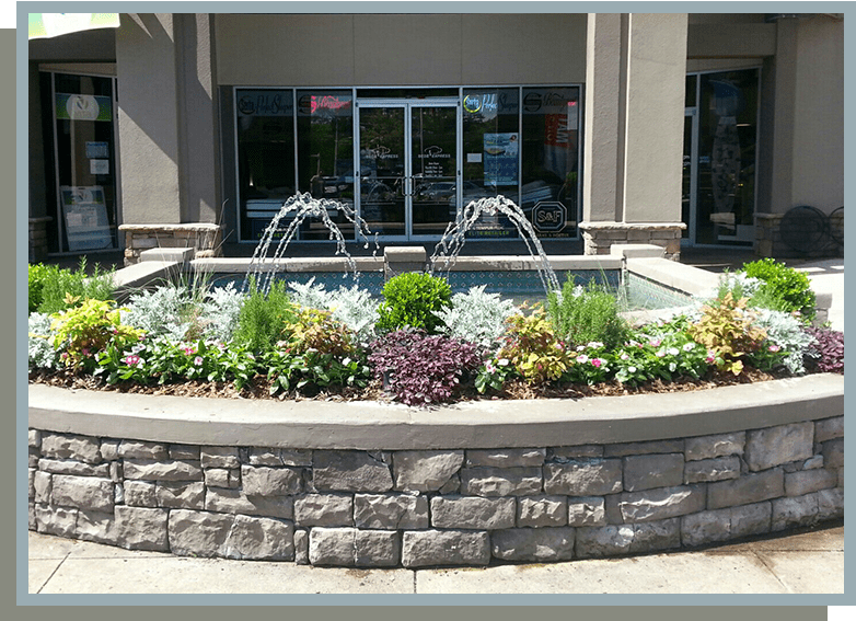 A fountain in front of a building with flowers.